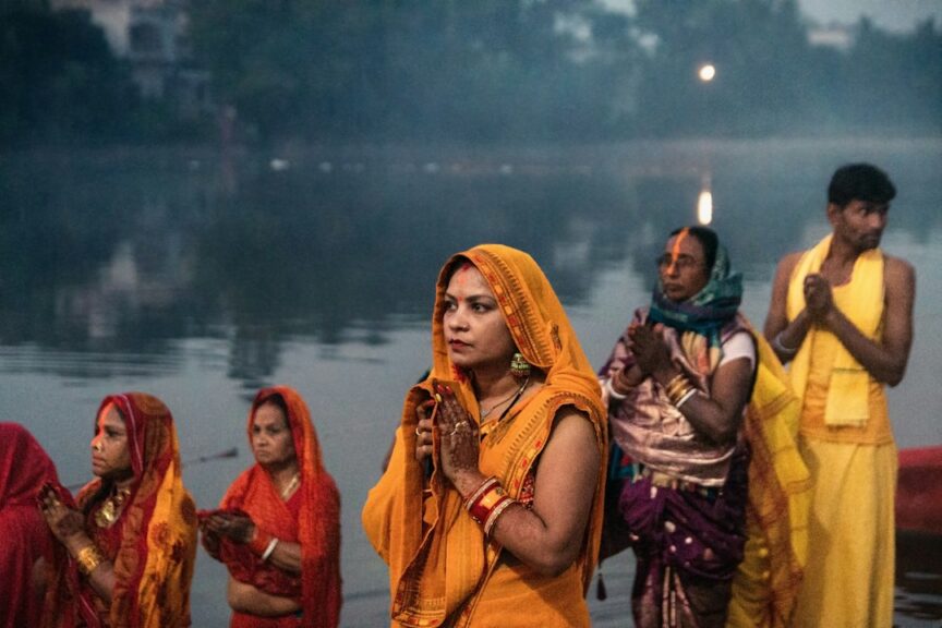 A group of women standing in front of a body of water during Chhath Puja