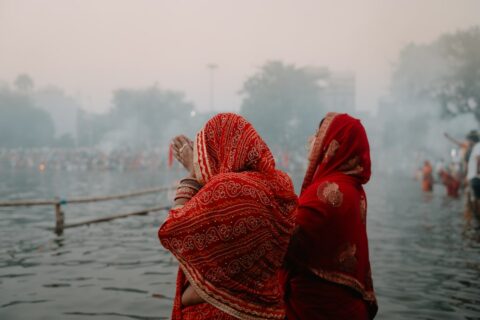 A woman in a red sari standing in a body of water during Chhath Puja