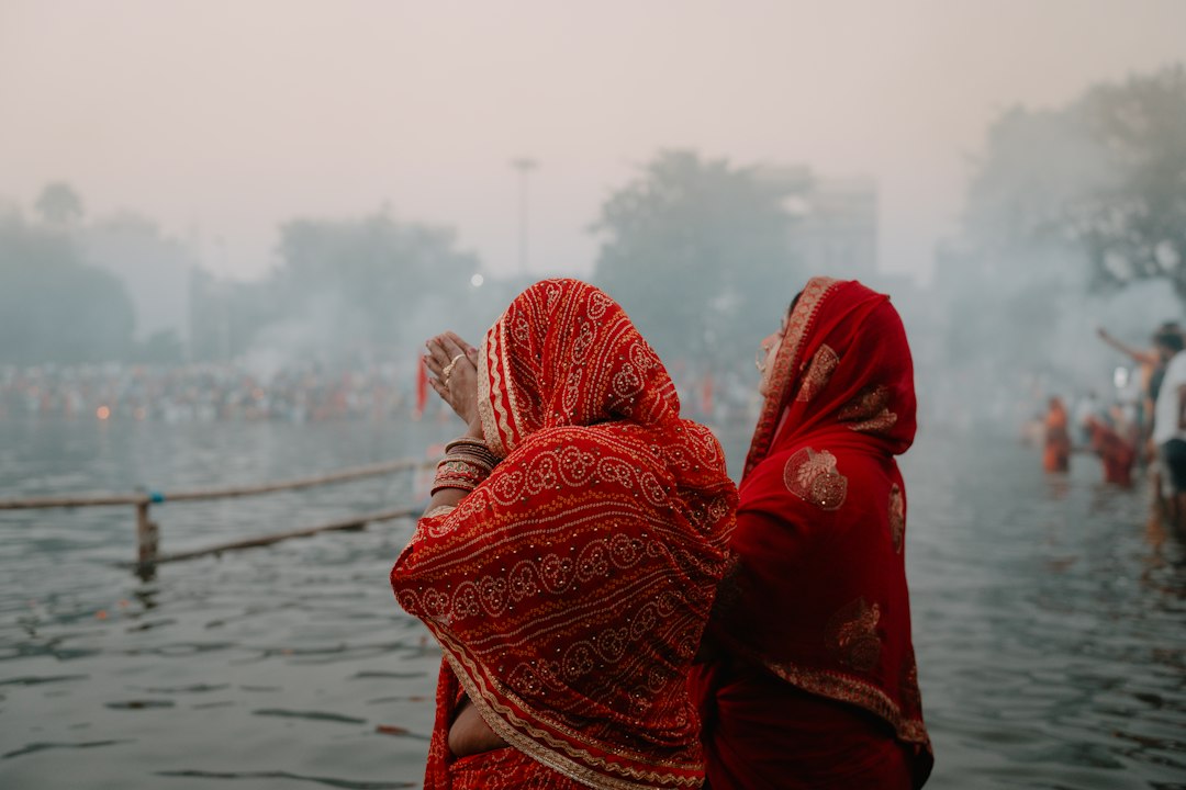 A woman in a red sari standing in a body of water during Chhath Puja